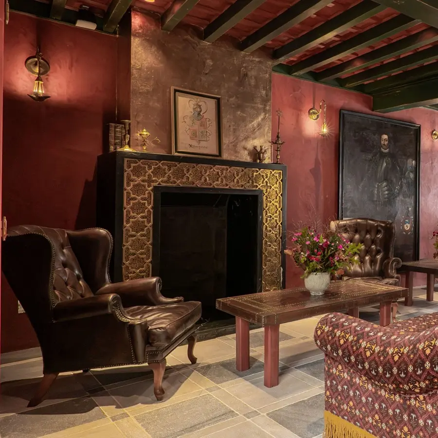 Sala de estilo barroco con chimenea, sillones y mesa con flores.