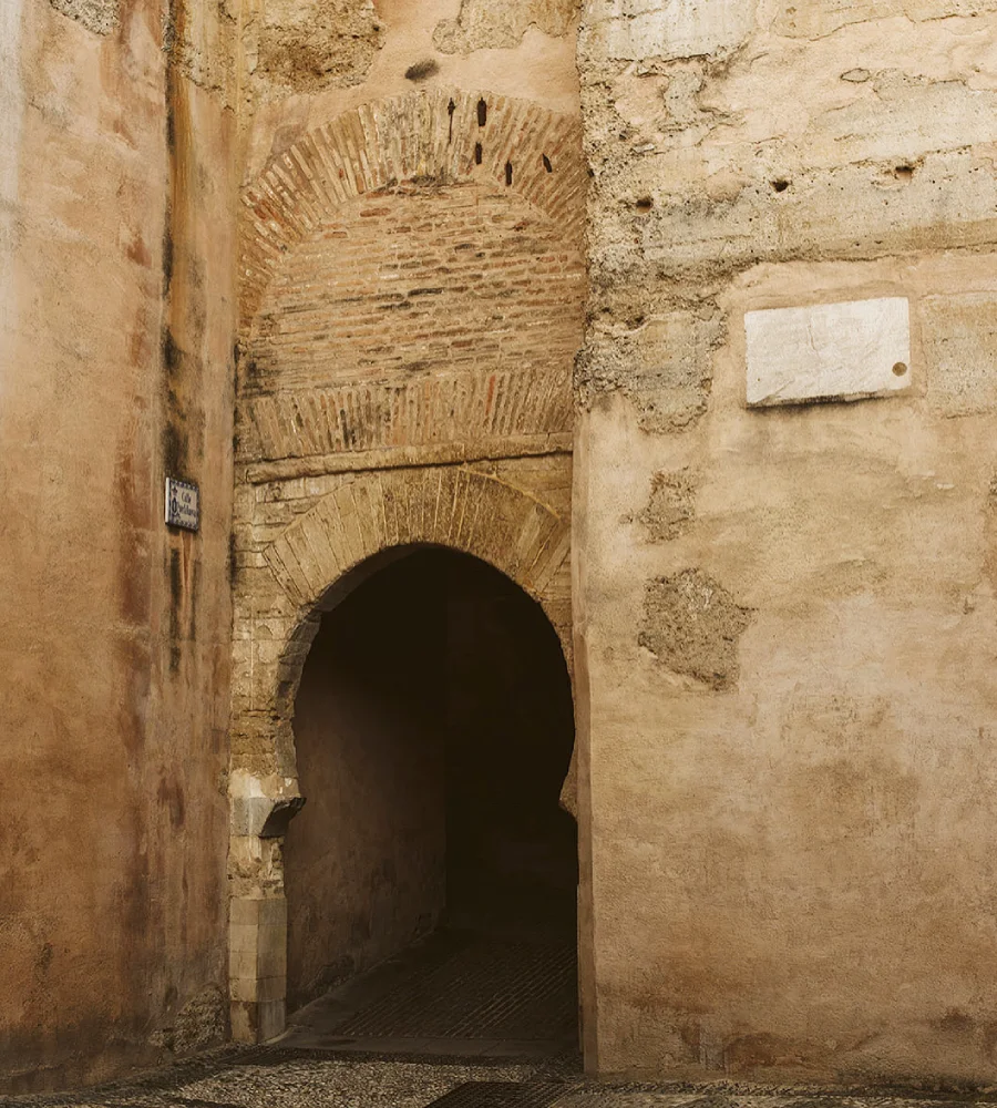 Pasillo con arco de piedra y paredes antiguas, con b&oacute;veda decorada.