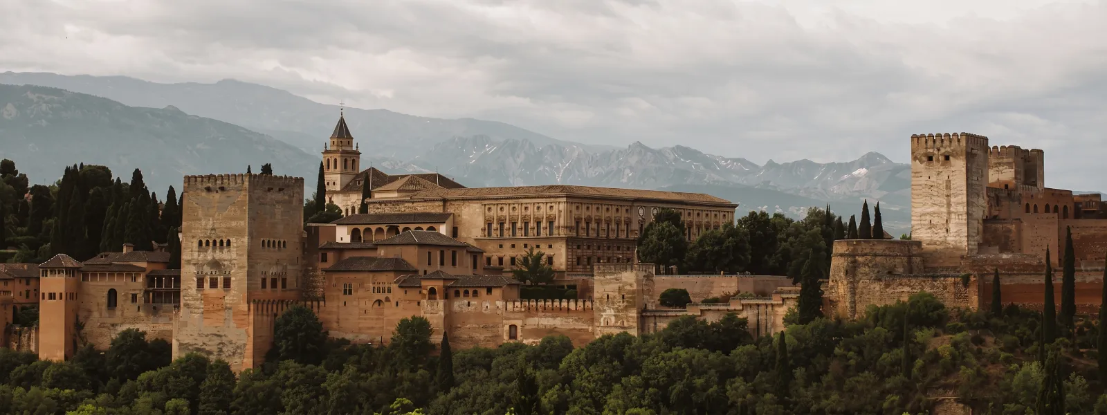Alhambra con torres y murallas, vista de monta&ntilde;as bajo cielo nublado