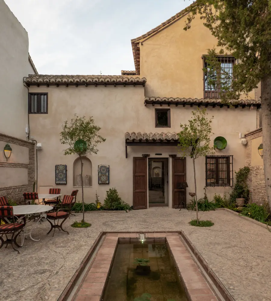 Patio andaluz con fuente de agua, plantas y mesas bajo paredes encaladas