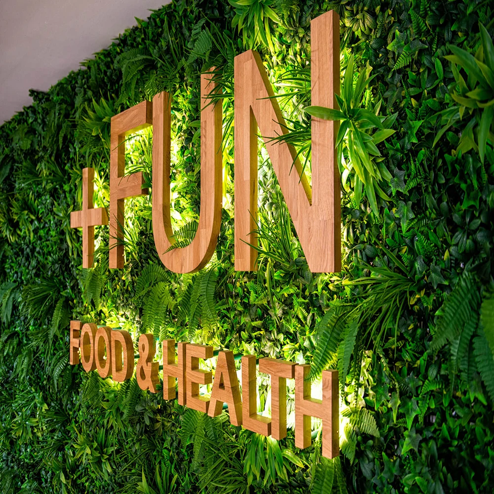 Logo &ldquo;JU&rdquo; y &ldquo;FOOD & HEALTH&rdquo; sobre un muro verde con plantas.