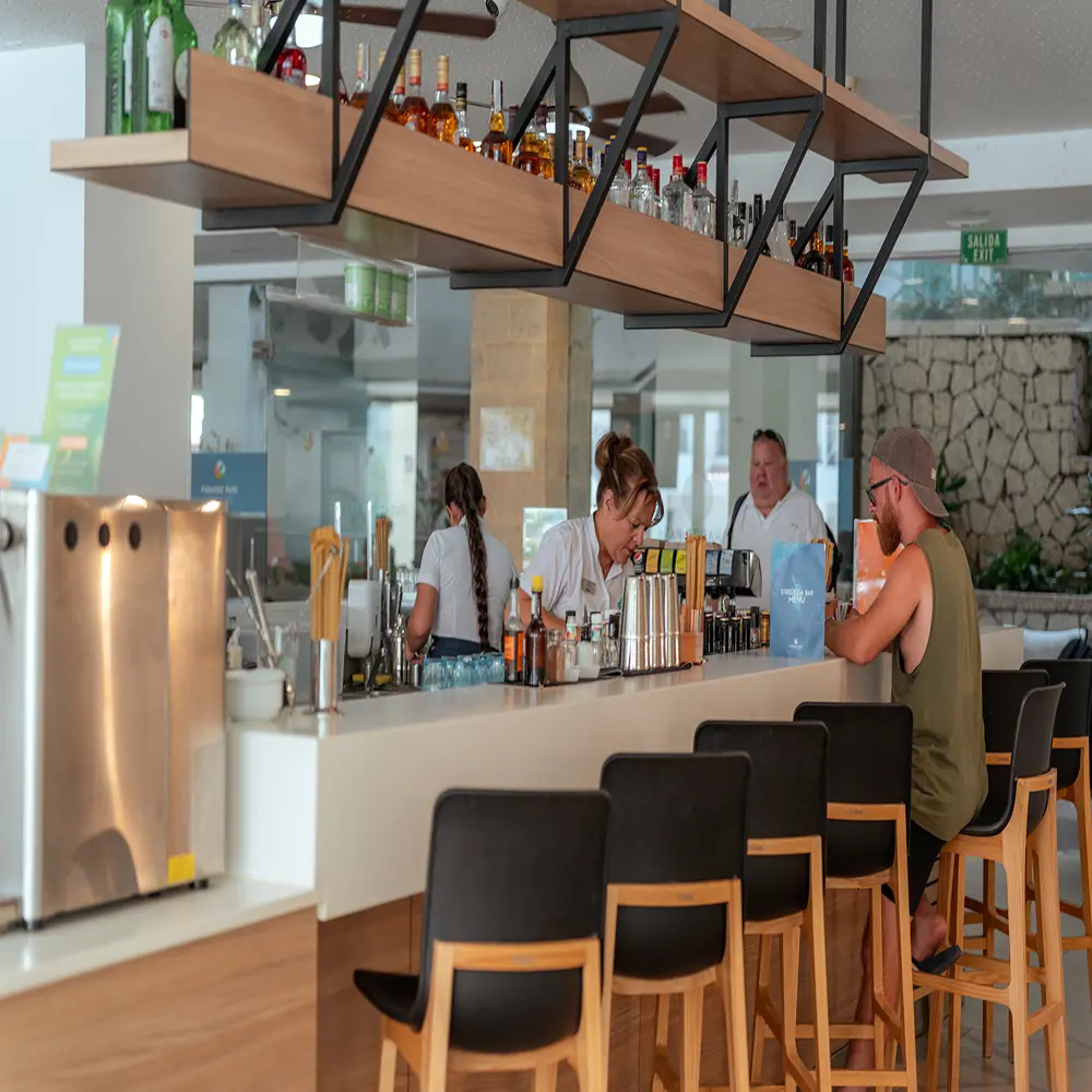 Barra de bebidas con personal y clientes en un bar moderno, botellas y estantes
