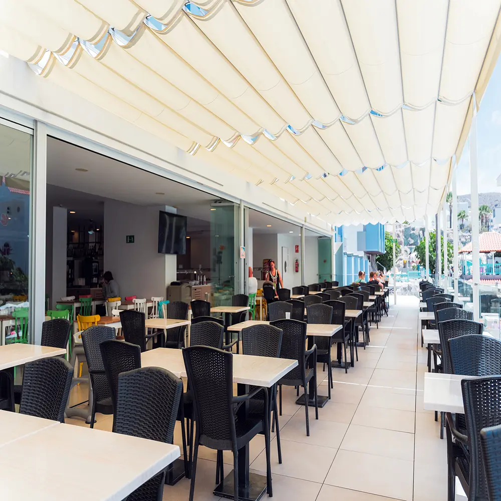 Terraza de restaurante con mesas y sillas bajo toldo blanco y azul