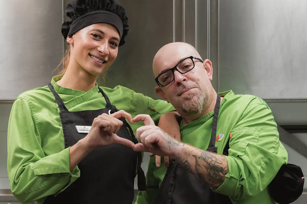 Dos trabajadores con uniformes verdes haciendo un corazón con las manos