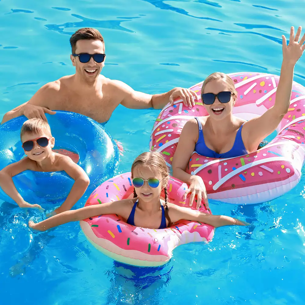Familia con gafas de sol flotando en piscina con anillos inflables donut rosa