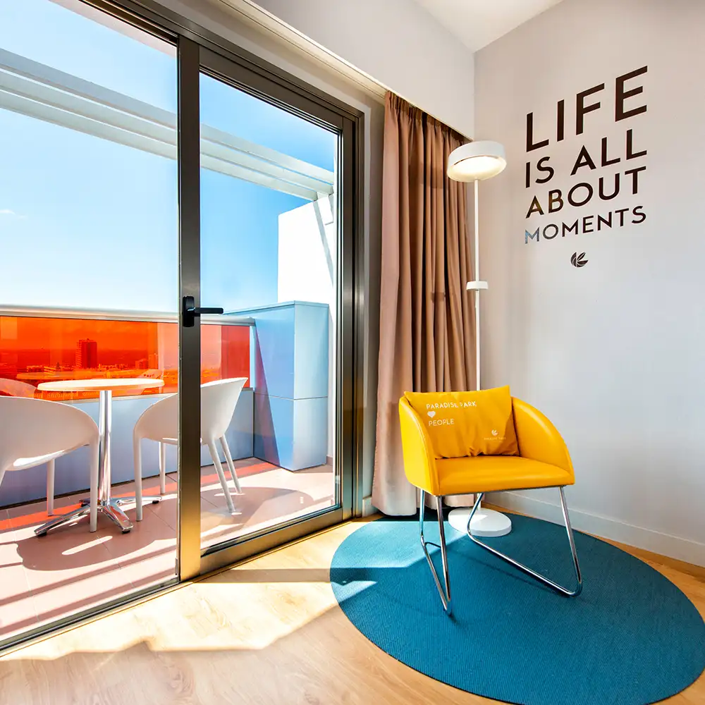Interior de oficina moderna con silla amarilla, luz y texto &ldquo;LIFE IS ALL ABOUT MOMENTS&rdquo;.