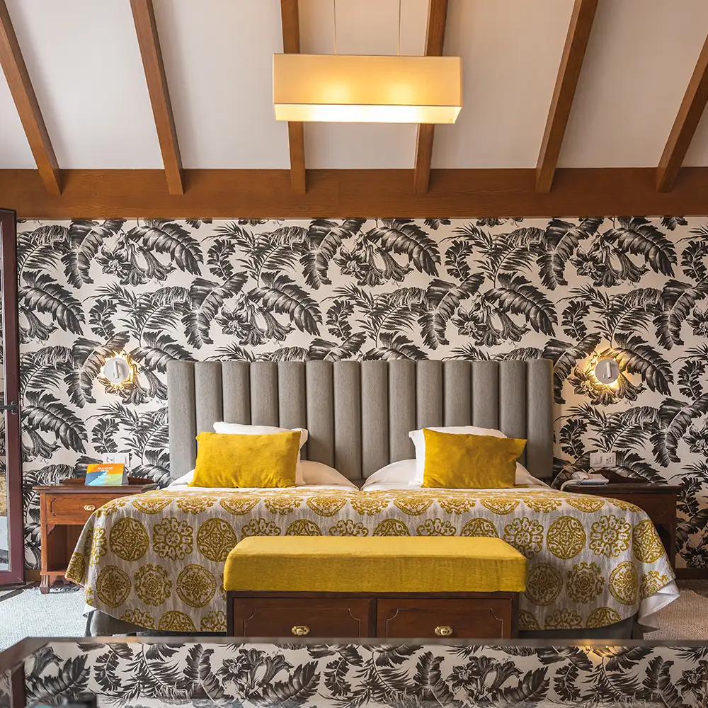 Dormitorio con cama, dos cojines amarillos y papel tapiz tropical en la pared