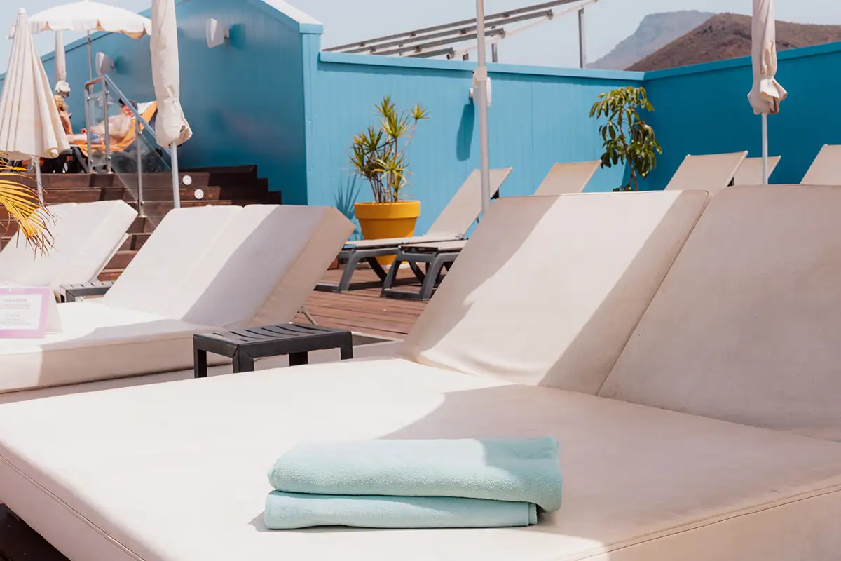 Terraza con tumbonas blancas, toallas y pared azul con plantas y monta&ntilde;as al fondo