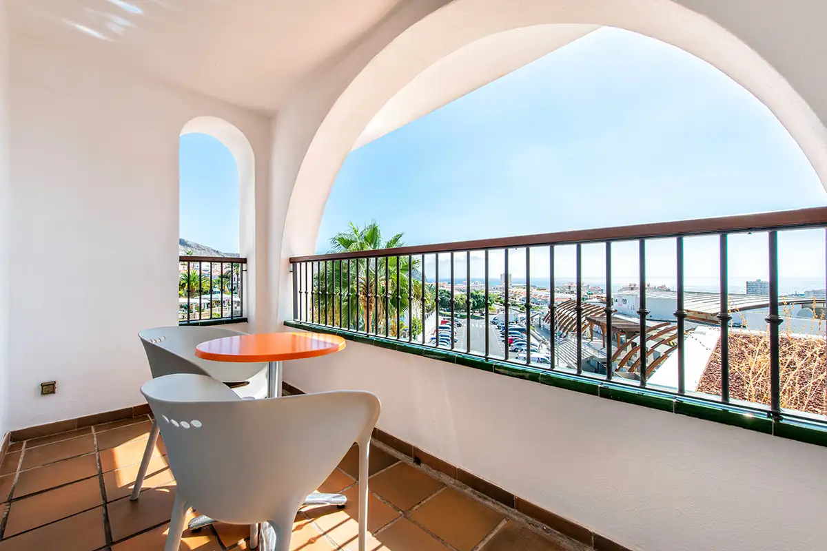 Terraza con mesa y sillas, barandilla verde y vista al mar y la ciudad.