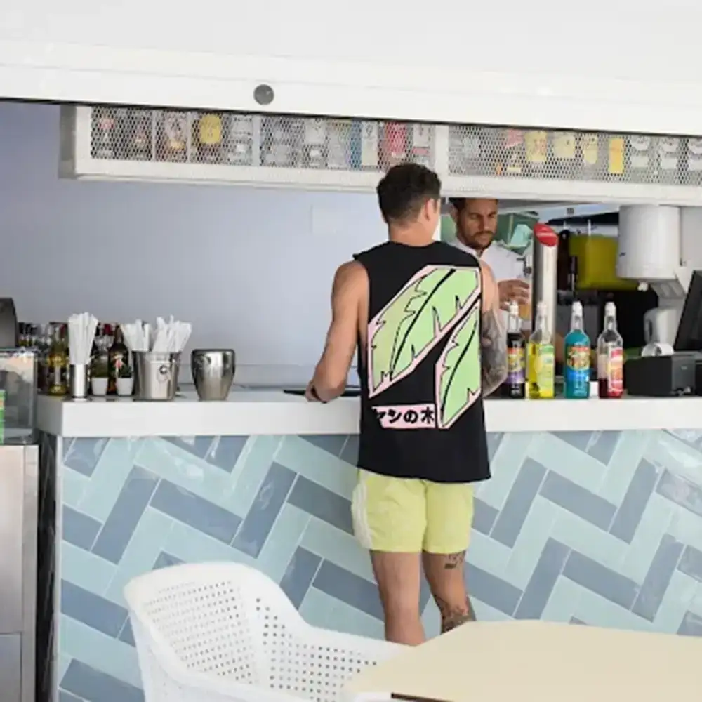 Camarero de espaldas en la barra con bebidas y botella de coctel.