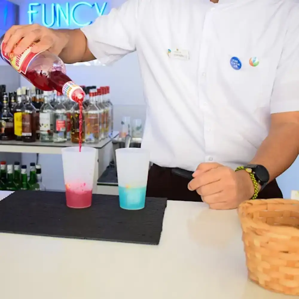 Barman vierte licor en vasos de c&oacute;ctel rosa y azul en una barra.