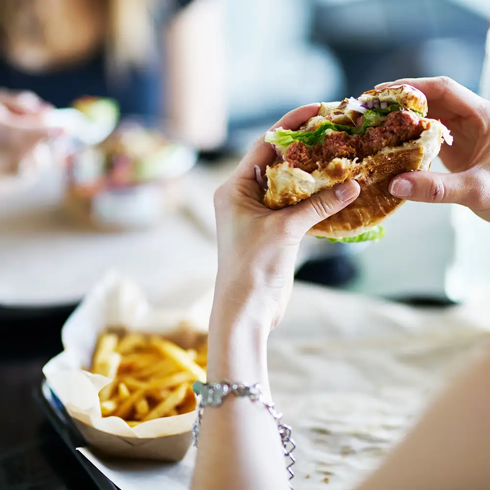 Manos sosteniendo un s&aacute;ndwich abierto con carne y lechuga; fondo desenfocado