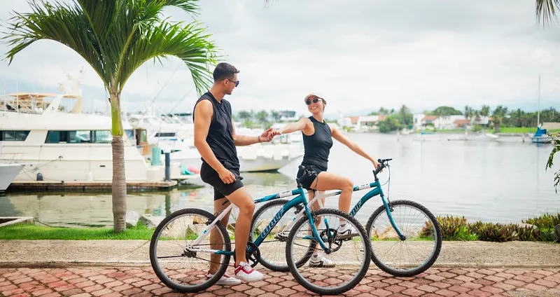 Couple riding a bike along the pier and yachts, in a tropical setting.