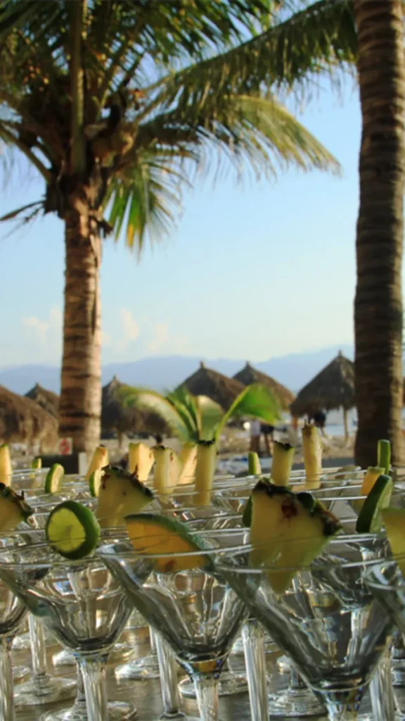 Copas y sombrillas en una mesa con palmeras y cielo azul al fondo