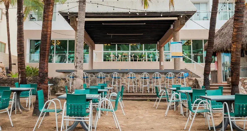 Terraza con palmeras, sillas verdes y blancas y escenario con barandales