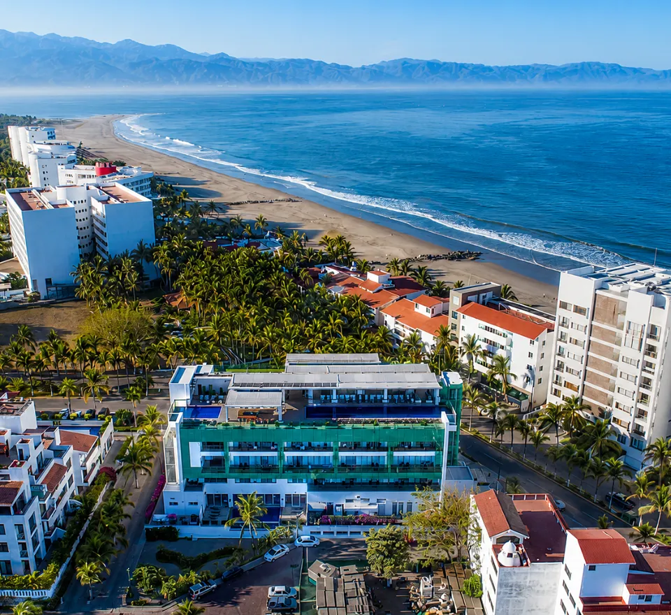 Vista a&eacute;rea de hotel frente a playa con palmeras y monta&ntilde;as al fondo