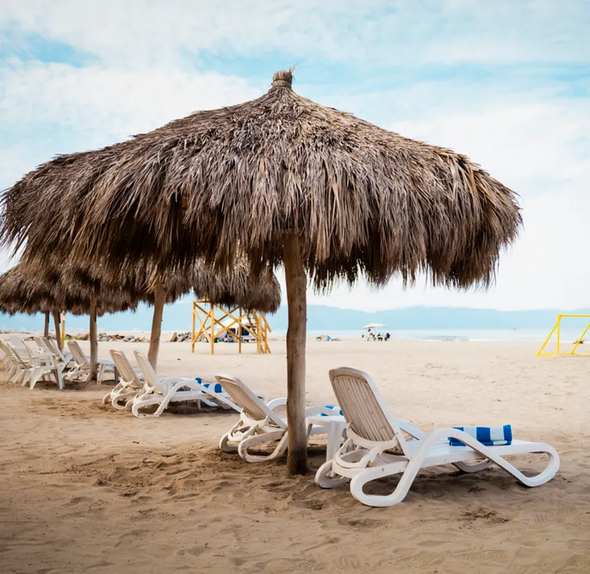Sombrillas de paja y tumbonas en una playa con cielo despejado