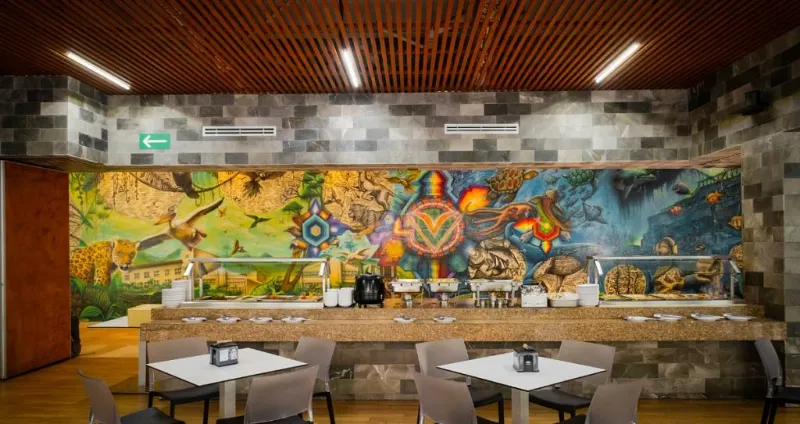 Interior de bar con mesas y barra decorada muralista, luz tenue y suelo de madera