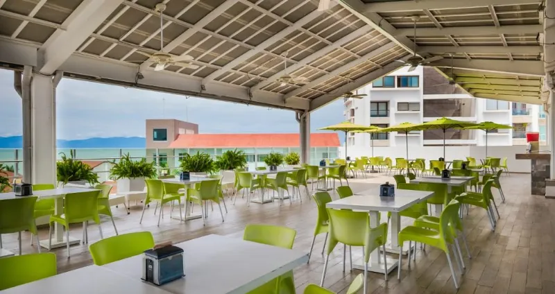 Terraza luminosa con mesas y sillas verdes bajo techo de metal y vidrio