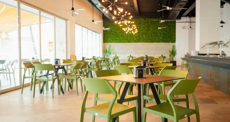 Comedor moderno con mesas verdes, sillas y luces colgantes en interior.