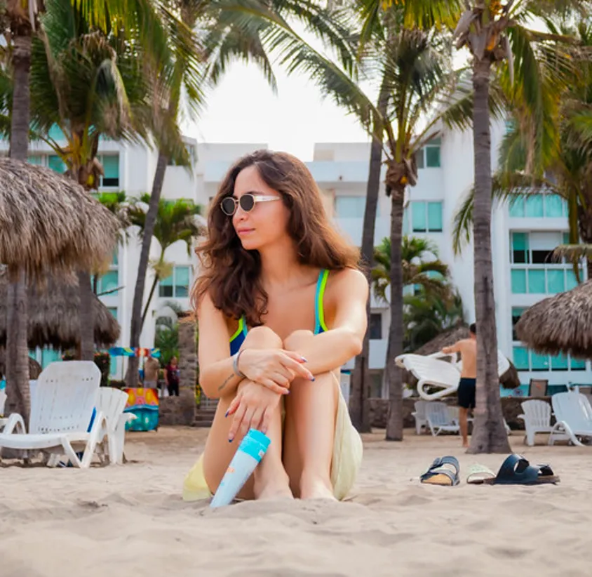 Mujer en traje de ba&ntilde;o bajo palmeras en la playa, tomando el sol.