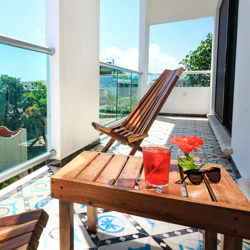 Terraza con mesa de madera, silla, flor roja y vaso en el balc&oacute;n