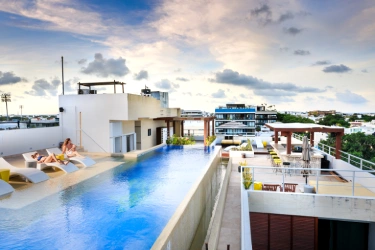 Pool in hotel with sun loungers, terrace, and view of cloudy sky at sunset.