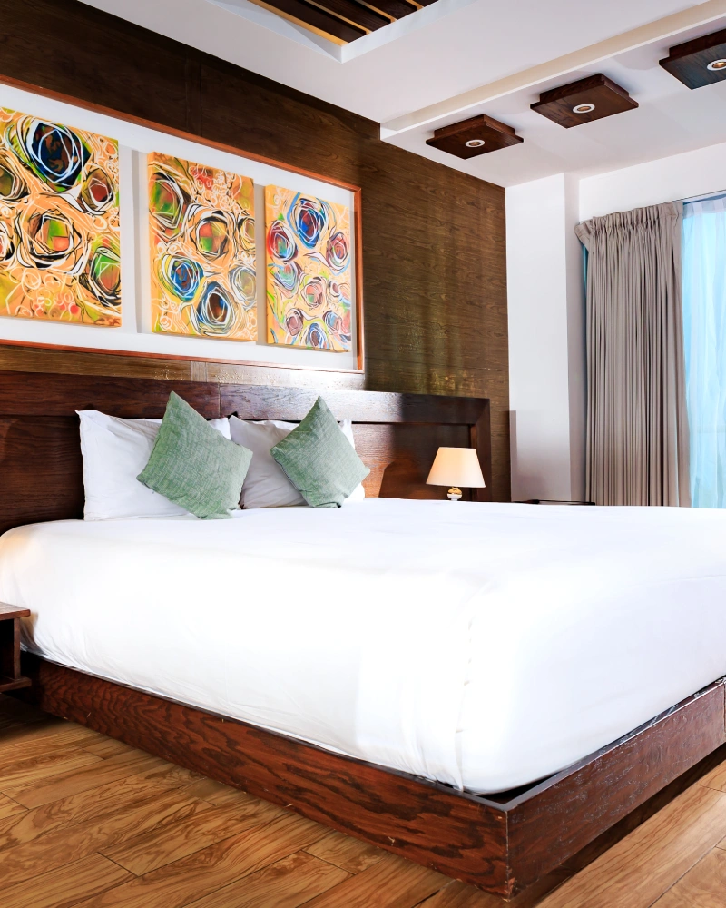 Modern bedroom with wooden bed, green pillows, and abstract paintings on the wall