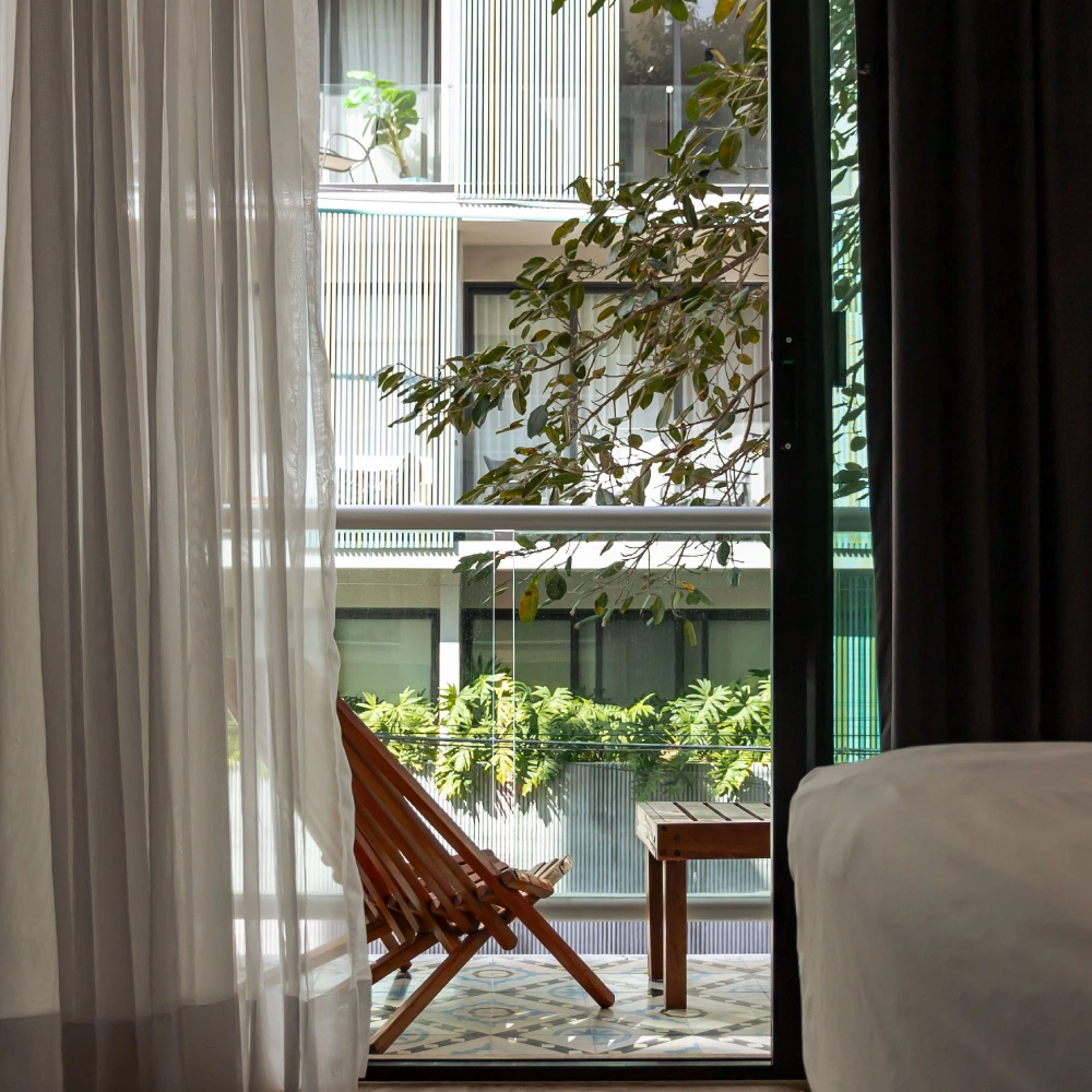 Ventana con cortina blanca, butaca y plantas verdes en interior moderno