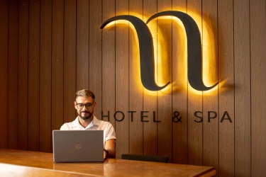 Hotel receptionist with laptop in front of sign 'HOTEL & SPA'