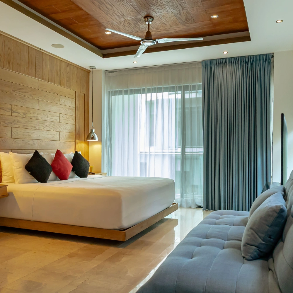 Dormitorio moderno con cama, sof&aacute; gris y cortinas junto a ventanal grande