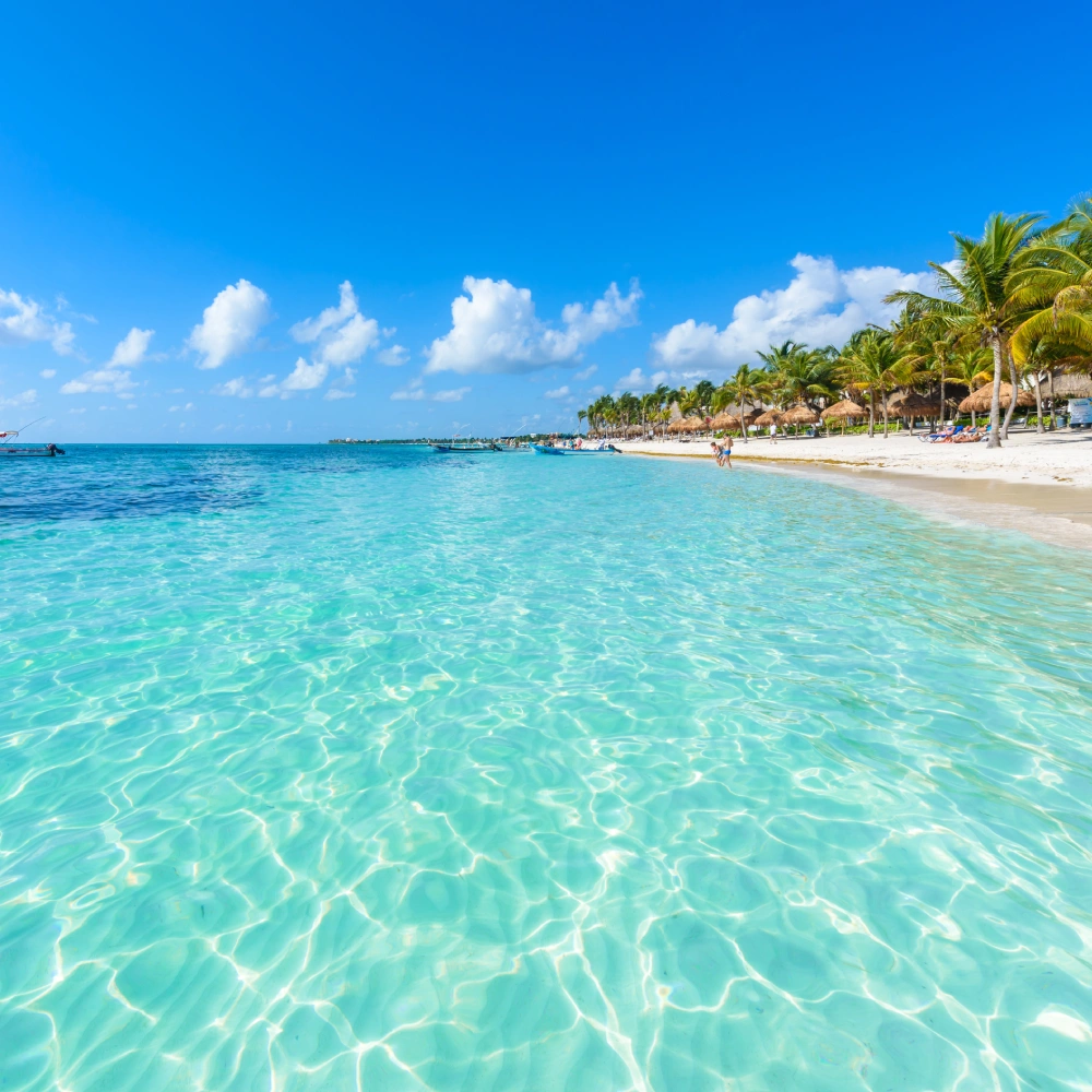 Playa tropical con palmeras, aguas turquesa y cielo azul con nubes.