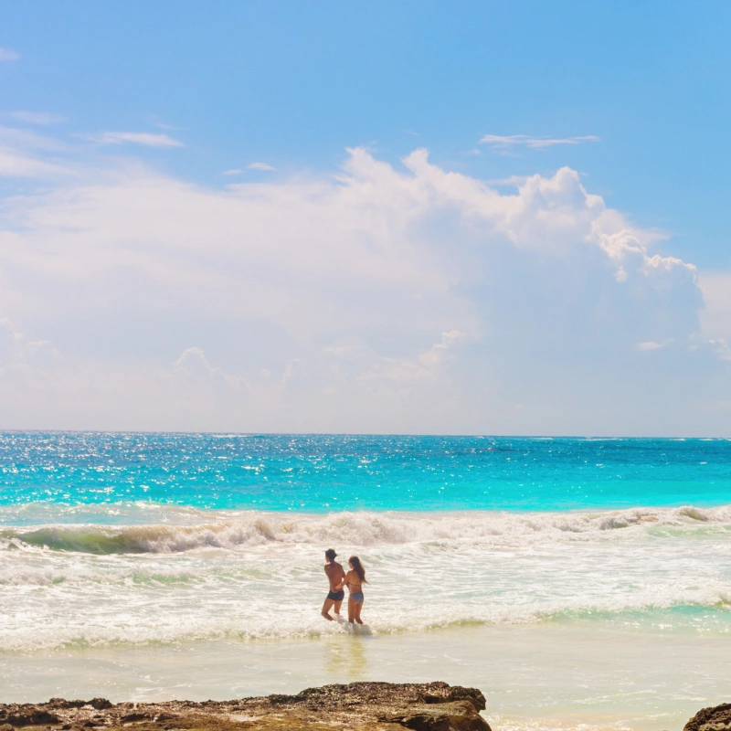 Couple walking on the beach with waves and blue sky, turquoise sea