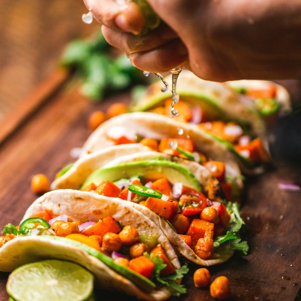 My hand serves tacos with vegetables, chickpeas, and lemon on a wooden board.