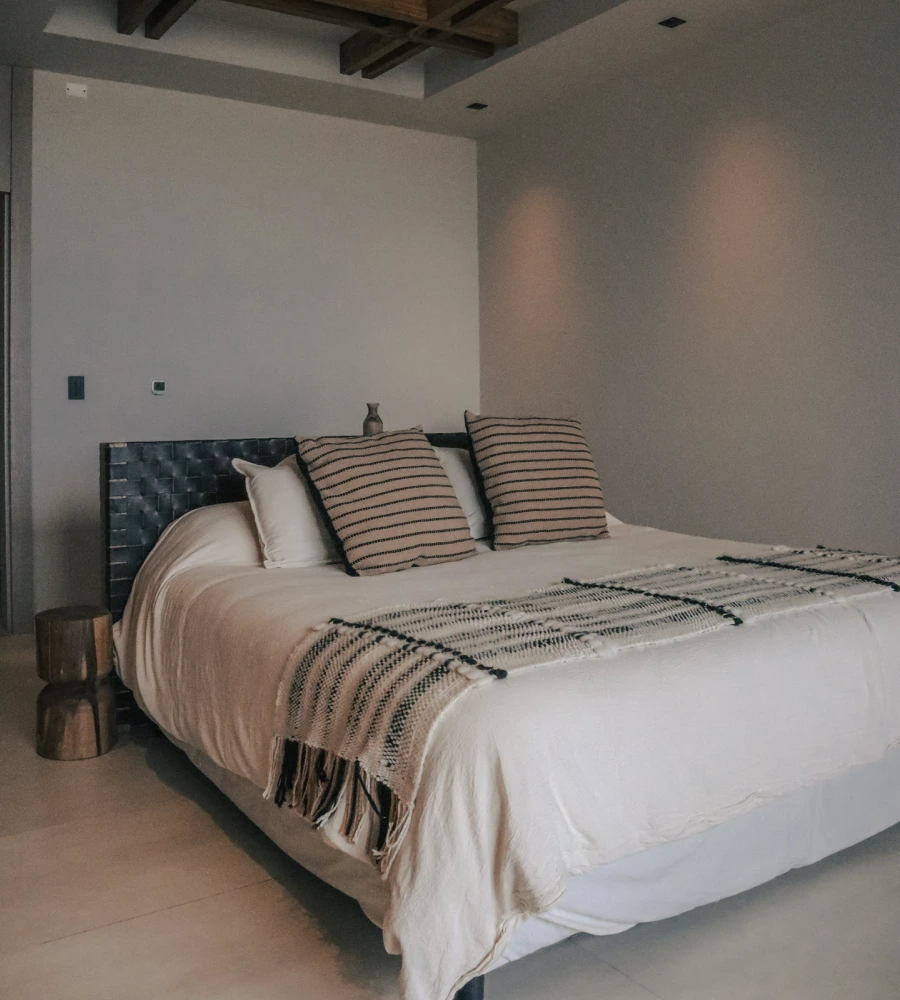 Cama con cabecero tapizado y cojines a rayas en un dormitorio minimalista