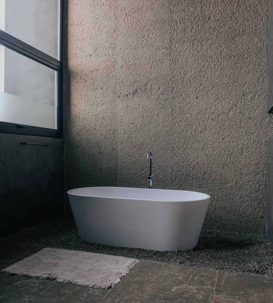 Ba&ntilde;era blanca ovalada en un ba&ntilde;o moderno con pared de textura gris