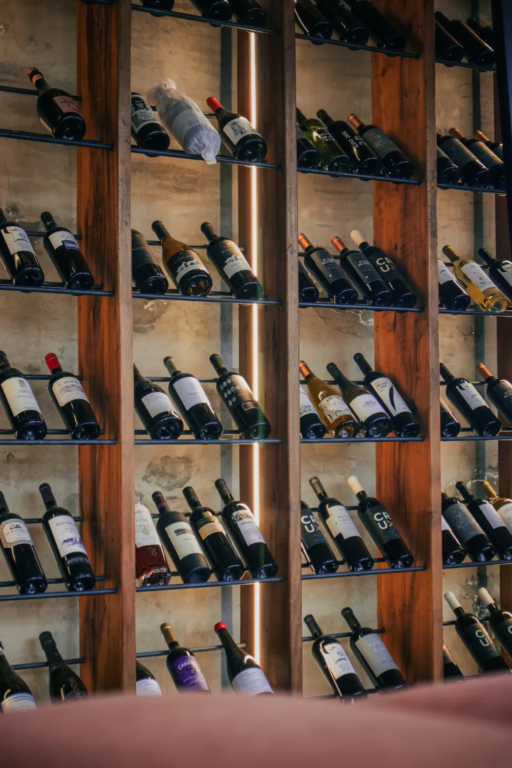 Estanter&iacute;a de botellas de vino iluminadas, tras madera, en bodega.