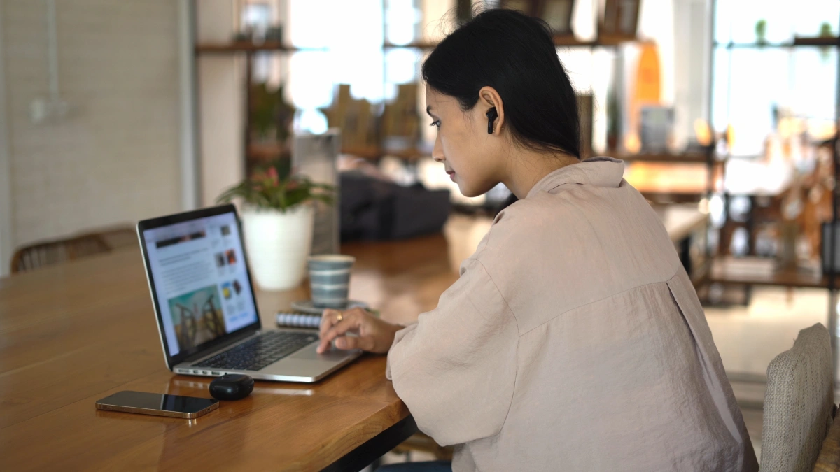 Mujer usando laptop en una oficina, con el m&oacute;vil sobre la mesa.