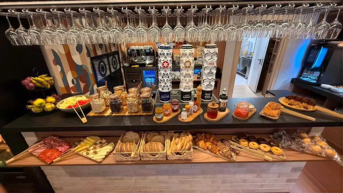 Buffet con botellas y bandejas de comida, frutas y dulces en mostrador.