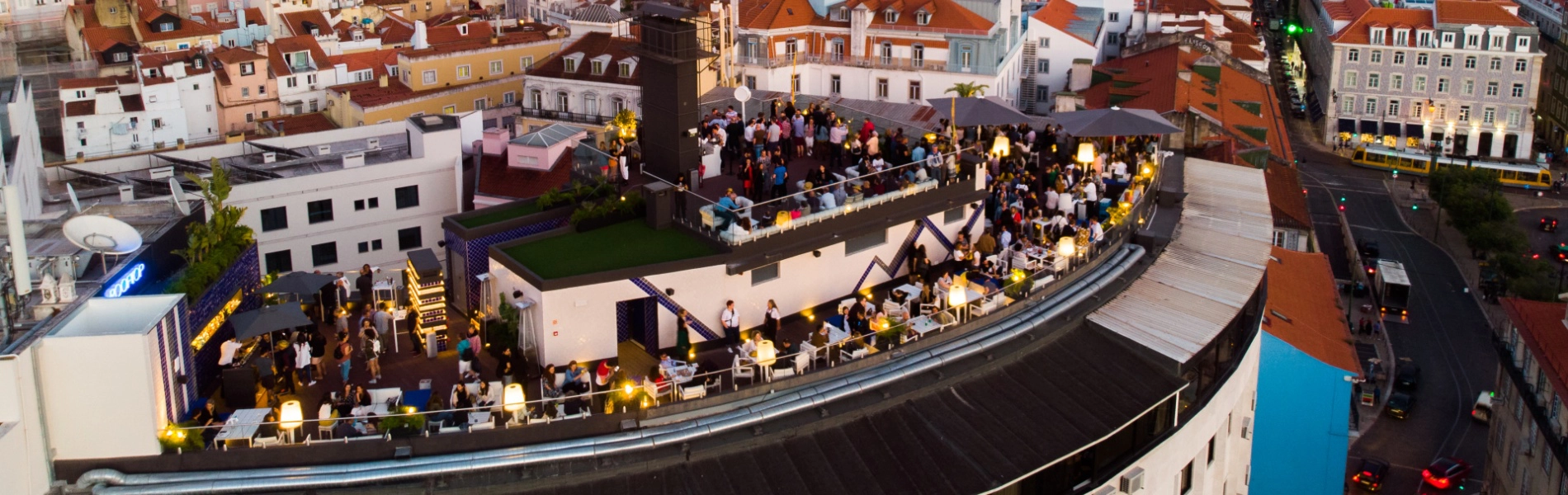 Luftaufnahme einer Terrasse mit Menschen, Lichtern und D&auml;chern in einer europ&auml;ischen Stadt