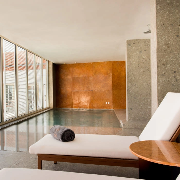 Modern spa area with indoor pool, lounge chairs and stone wall.