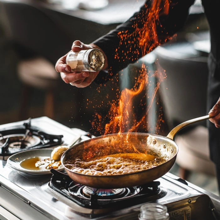 Chef sprinkling spicy seasoning on a skillet on an industrial stove