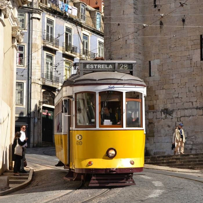 Tram amarillo en calle estrecha con edificio de piedra y placa &ldquo;ESTRELA 28&rdquo;