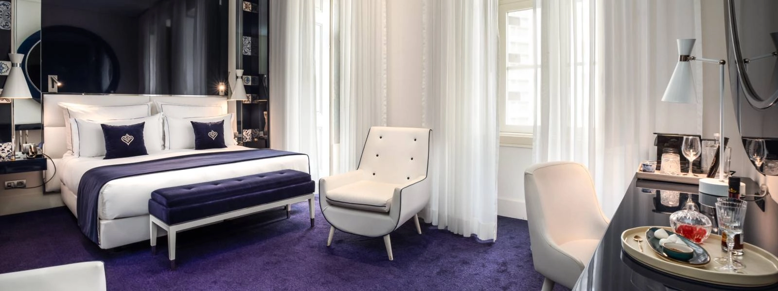 Modernes Hotelzimmer mit Bett, hellen Sesseln und wei&szlig;en Vorh&auml;ngen.