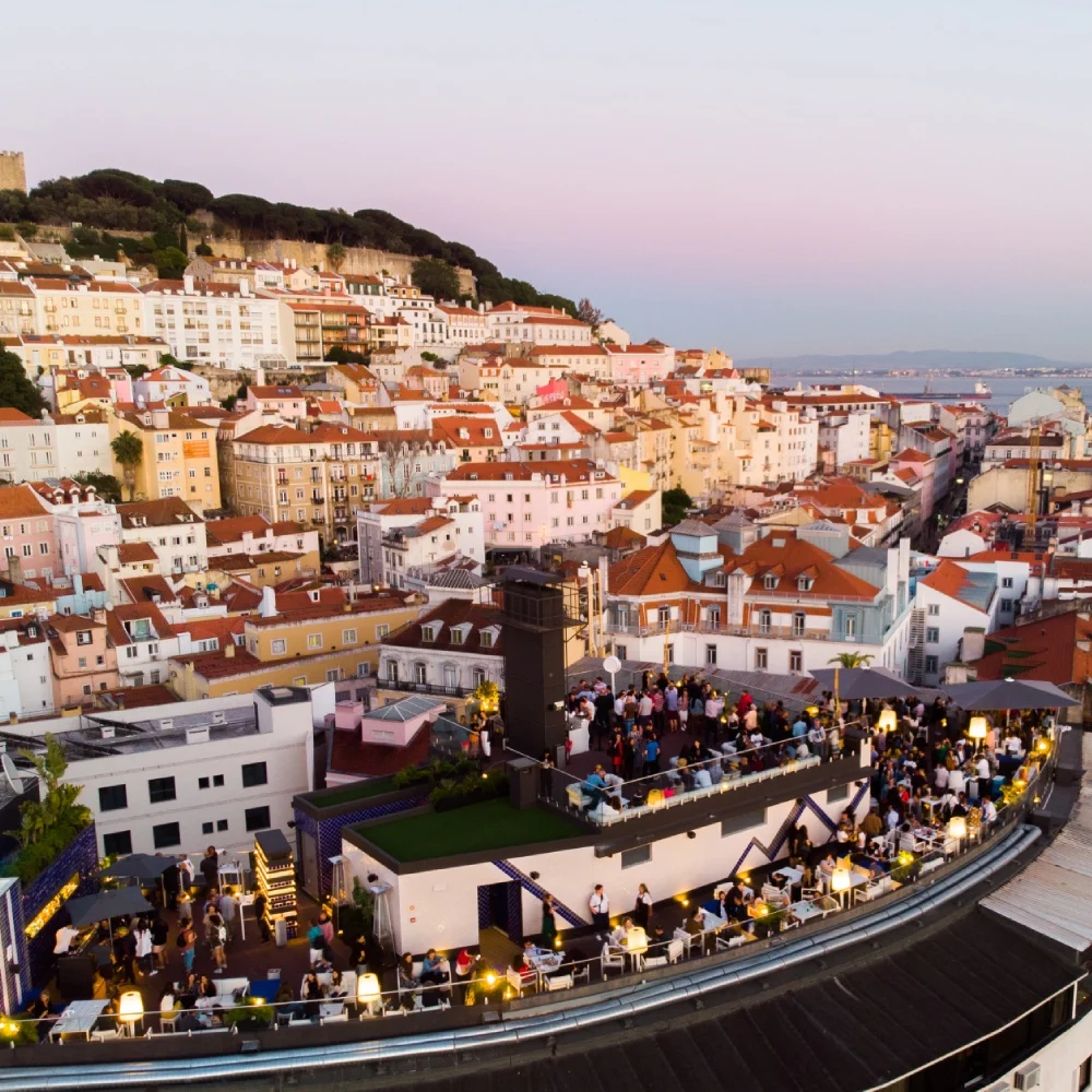 View of the city with colorful houses and a terrace with people at sunset.