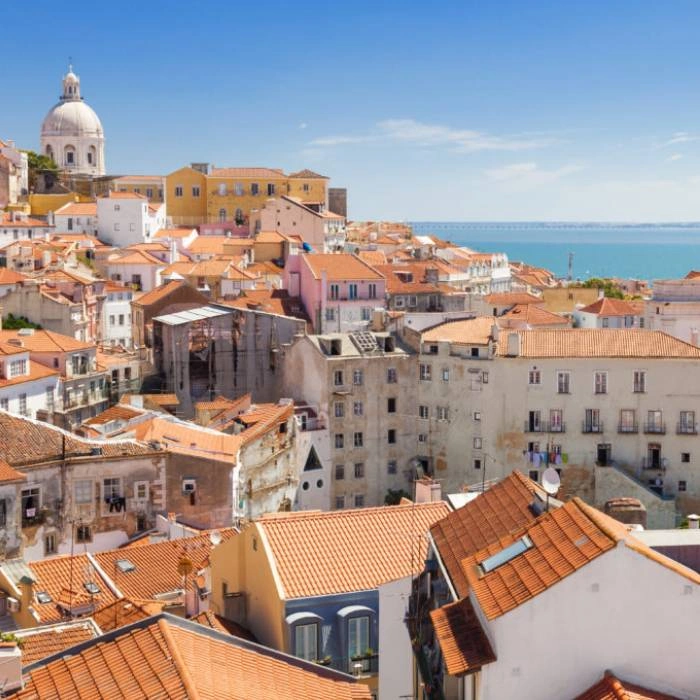 Vista panor&aacute;mica de tejados coloridos y mar al fondo en Lisboa.