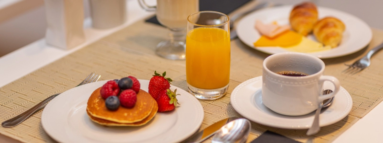 Fr&uuml;hst&uuml;ck mit Pfannkuchen, Obst, Saft und Kaffee auf gedecktem Tisch