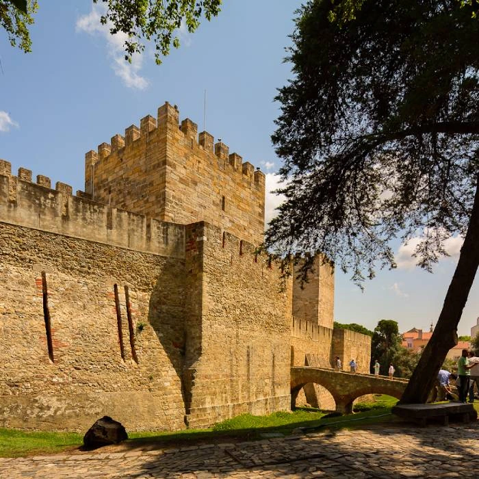 Muralla medieval de piedra con &aacute;rboles y personas en el jard&iacute;n al lado