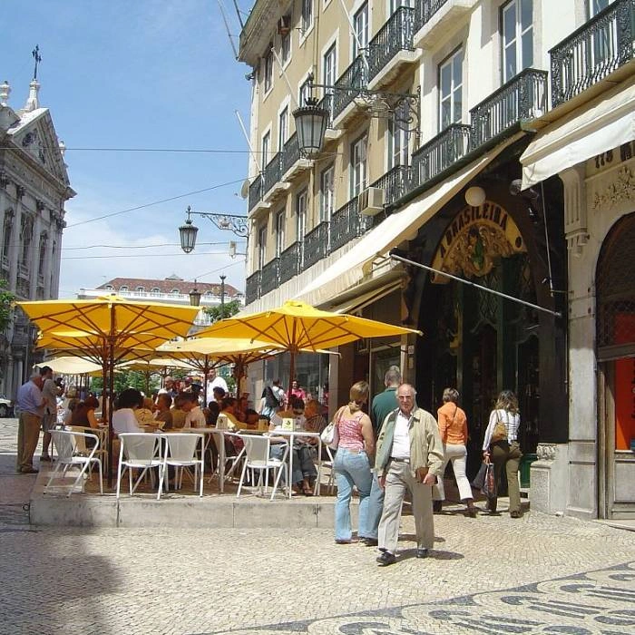 Calle con mesas al aire libre, personas y sombrillas amarillas en Lisboa