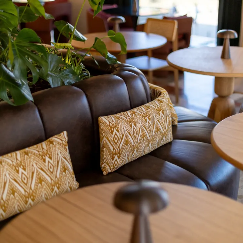 Sof&aacute; de couro com almofadas estampadas, plantas e mesas em um caf&eacute;.